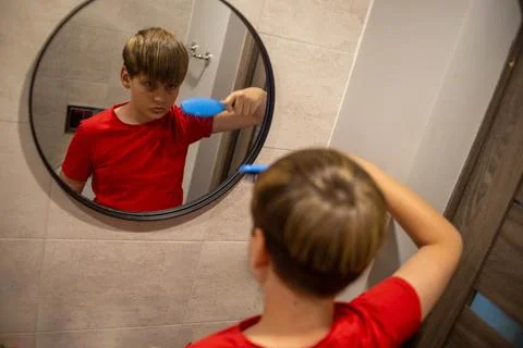 Boy Brushing Hair While Looking In Bathroom Mirror Stock Photos