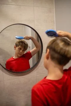 Boy Brushing Hair While Looking In Bathroom Mirror Stock Photos