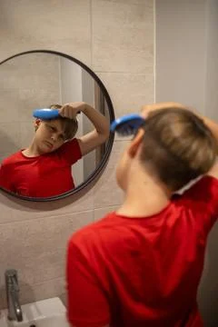 Boy Brushing Hair While Looking In Bathroom Mirror Stock Photos