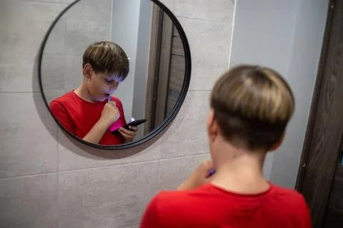 Boy Brushing Teeth While Using Smartphone In Mirror Stock Photos