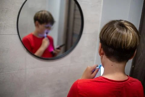 Boy Brushing Teeth While Using Smartphone In Mirror Stock Photos
