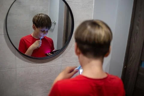 Boy Brushing Teeth While Using Smartphone In Mirror Stock Photos