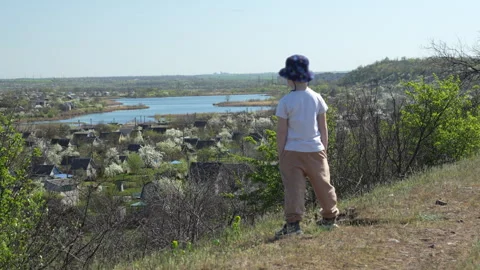 Boy in bucket hat looking at scenic rural landscape with river from hilltop Stock Footage 310536149