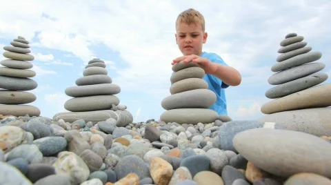 Boy building stone stack on pebbles, sky in background Stock Footage 598770