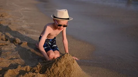 Boy builds sand castle on sandy beach at tropical resort, watching incoming Video stock 331245544