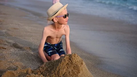 Boy builds sand structure; child builds sand castle at sunset on beach, creating Video stock 328173229