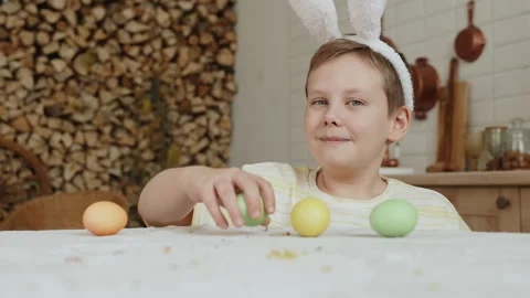 Boy with bunny ears headband pulls Easter colored egg from table. Stock Footage 262362796