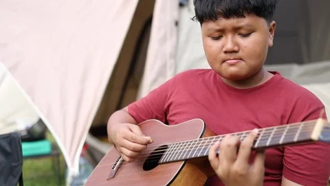 A boy is busy playing the guitar with concentration, sitting relaxed in the 動画素材 338425082