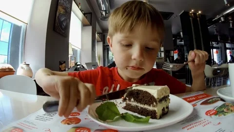 A boy at cafe is eating cheesecake by fork and table-knife. Stock Footage 147833983