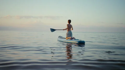 The boy calmly rows across the quiet water, against the backdrop of a golden Stock-Footage 318475917