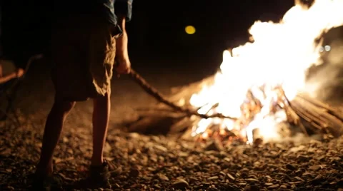 Boy at campfire on beach plays with stick Stock Footage 62442896