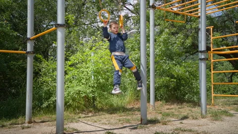 The boy can be seen pulling himself up on the rings on the playground Stock Footage 274421019