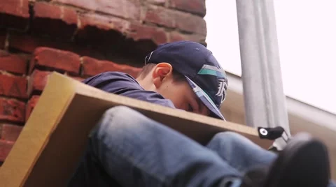 The boy in the cap draws on an easel sitting on the stone stairs in the sky Stock Footage 54939347