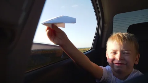 Boy in a car window with a paper plane. Family trip. Children's games and dreams 库存影片 121529376