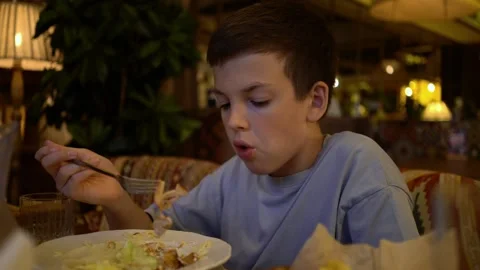 Boy carefully eats fresh salad with fork at cozy restaurant table Video stock 342193639