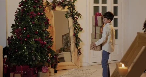 A boy carries a stack of gifts to the Christmas tree Stock Footage 221805663