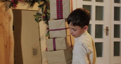 A boy carries a stack of gifts to the Christmas tree Stock Footage 221805892
