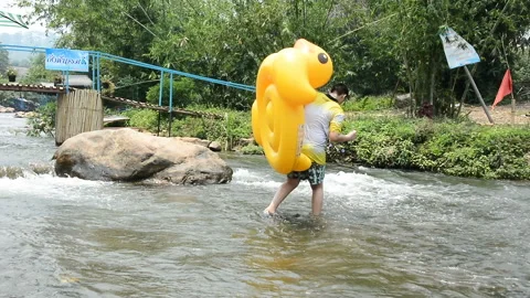 Boy carring plastic duck balloon across down stream Stock Footage 132581349