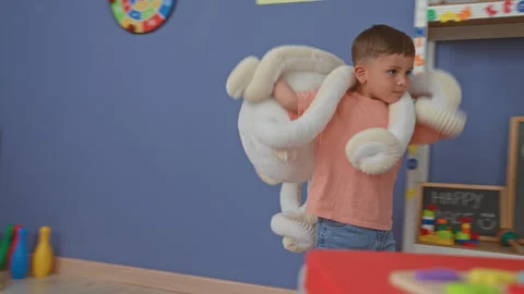 Boy carrying large white plush toy across a preschool playroom inside a bui.. Stock Footage 339234251