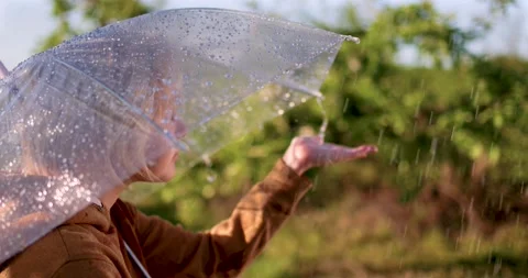 Boy catching the rain drops, that are falling from umbrella in spring garden Stockbeeldmateriaal 154911097