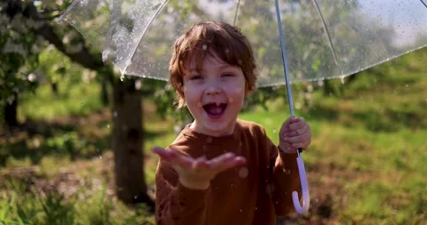 Boy catching the rain drops, that are falling from umbrella in spring garden Stockbeeldmateriaal 154911101