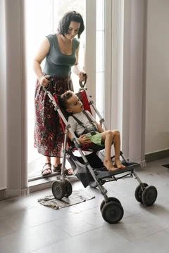 Boy with Cerebral Palsy in special chair going outside with mother. Access Stock Photos