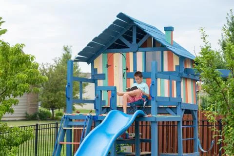 Boy on chair reading while seated on playhouse Stock Photos