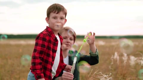 Boy in checkered shirt blows bubbles with mother help on freshly mowed field Stock Footage 254300828
