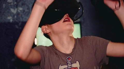 The boy cheerfully makes movements with his hands with a VR helmet on his head Stock Footage 145674804