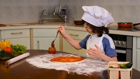 Boy with chef hat spreading tomato sauce on pizza base Stock Footage 125563170