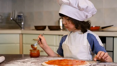Boy with chef hat spreading tomato sauce on pizza base Stock Footage 125563536