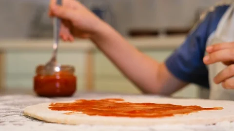 Boy with chef hat spreading tomato sauce on pizza base Stock Footage 125564001