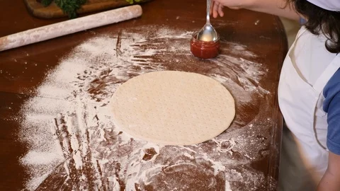 Boy with chef hat spreading tomato sauce on pizza base Stock Footage 125564216