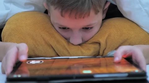 Boy child lying on bed watching cartoons on digital tablet. Close-up portrait of Stock Footage 231343186