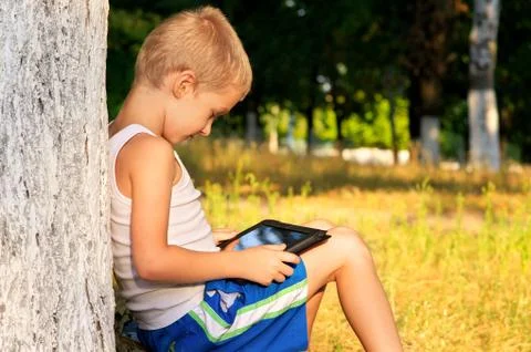 Boy child playing with tablet pc outdoor with forest on background computer g Stock Photos
