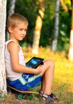 Boy child playing with tablet pc outdoor with forest on background computer g Stock Photos