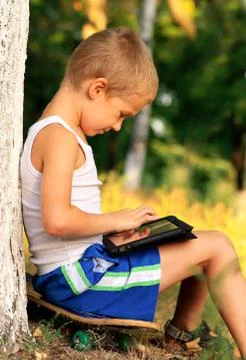 Boy child playing with tablet pc outdoor with forest on background computer g Stock Photos