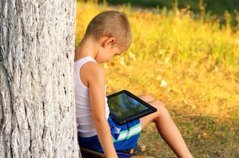 Boy child playing with tablet pc outdoor with forest on background computer g Stock Photos