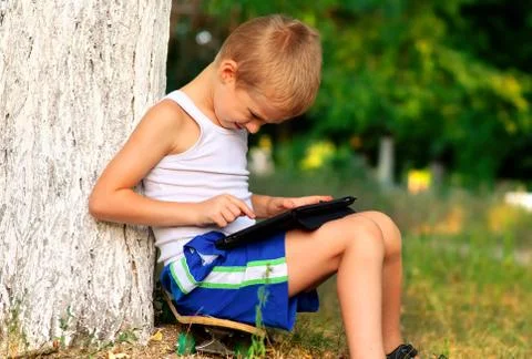 Boy child playing with tablet pc outdoor with forest on background computer g Stock Photos