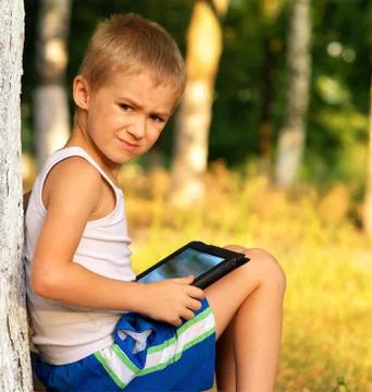 Boy child playing with tablet pc outdoor with forest on background game depen Stock Photos
