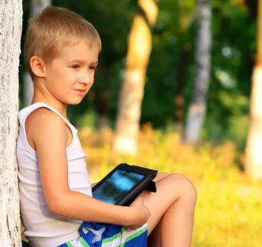 Boy child playing with tablet pc outdoor with forest on background game depen Stock Photos