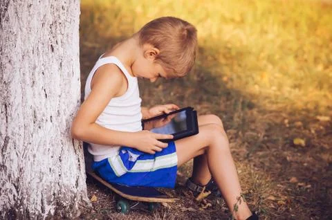 Boy child playing with tablet pc outdoor with summer nature on background com Stock Photos