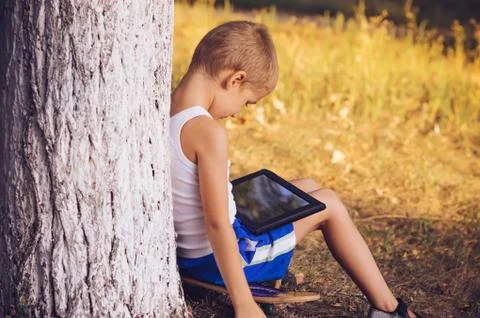 Boy child playing with tablet pc outdoor with summer nature on background com Stock Photos
