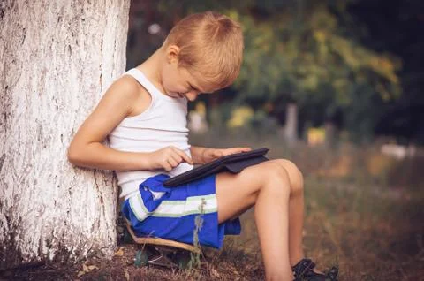 Boy child playing with tablet pc outdoor with summer nature on background com Stock Photos