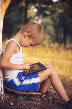 Boy child playing with tablet pc outdoor with summer nature on background com Stock Photos