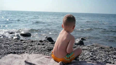 A boy-child sits with his back to the camera and throws a small pebble into the Stock Footage 171125375