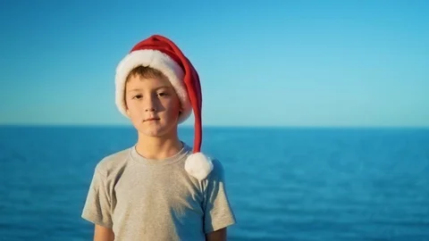A boy in a Christmas hat is standing against the sea and smiling Stock Footage 102367384