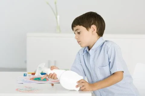 Boy cleaning crayon scribbles off of table, holding spray bottle Stock Photos