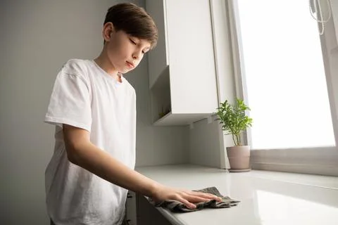 Boy cleaning kitchen surface learning household chores Stock Photos