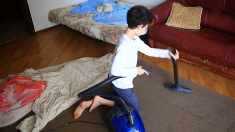 The boy cleans the carpet in the room with a vacuum cleaner Stock Footage 75875095